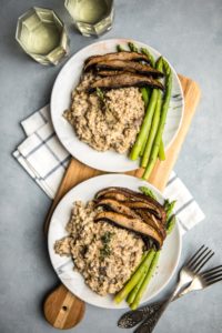 two plates of mushroom risotto with roasted mushrooms and asparagus on wood serving board