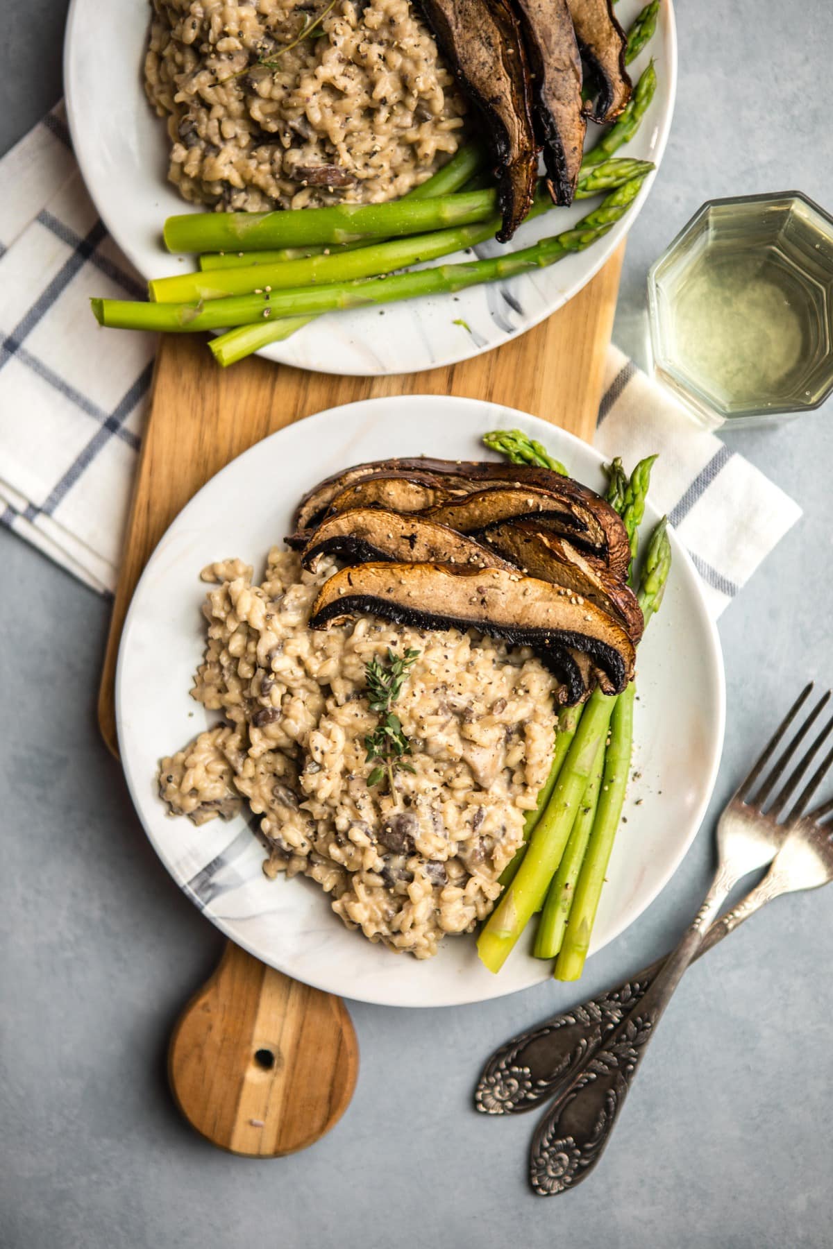 white plate of mushroom risotto with roasted mushrooms and asparagus on wood serving board