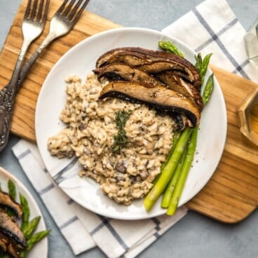 mushroom risotto with fresh asparagus and roasted mushroom caps on white plate on wood cutting board