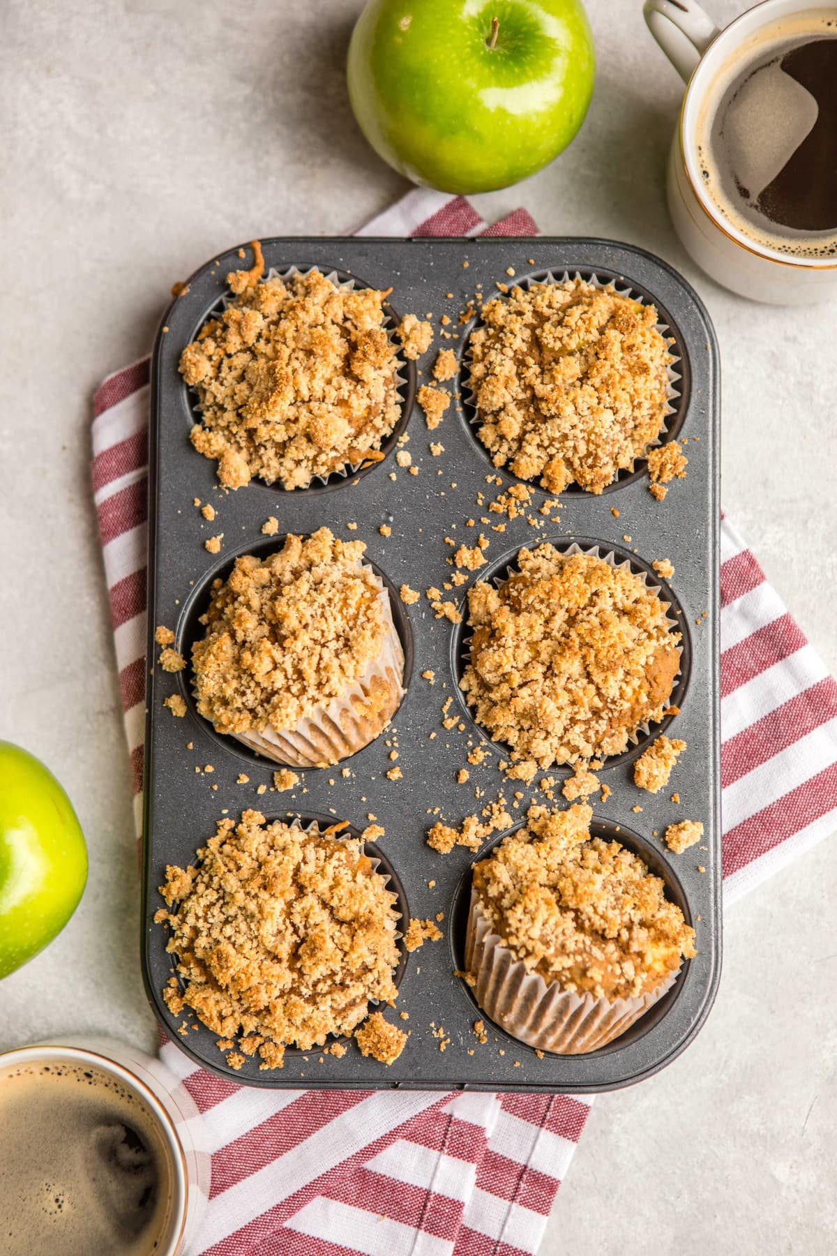 tray of baked apple cinnamon muffins with cups of coffee and fresh apples on light gray background