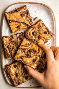 hand grabbing chocolate peanut butter brownie off of white serving tray