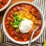 vegan chili in white bowl topped with vegan sour cream and green onions