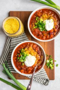 two bowls of vegan chili on wooden cutting board topped with vegan sour cream and green onion