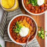 two bowls of vegan chili topped with vegan sour cream, green onion, and nutritional yeast