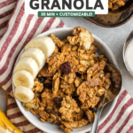 small white bowl of vegan granola with fresh banana slices and silver spoon