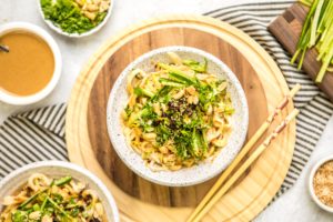 white speckled bowl of sesame noodles topped with cucumber, green onions, and chili oil