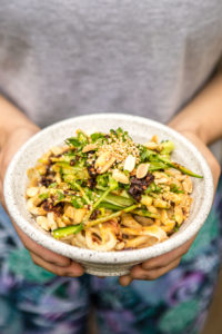 white speckled bowl of sesame noodles topped with green onion, peanuts, and chili oil