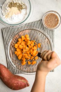 mashing cubed sweet potatoes in large glass bowl on white background