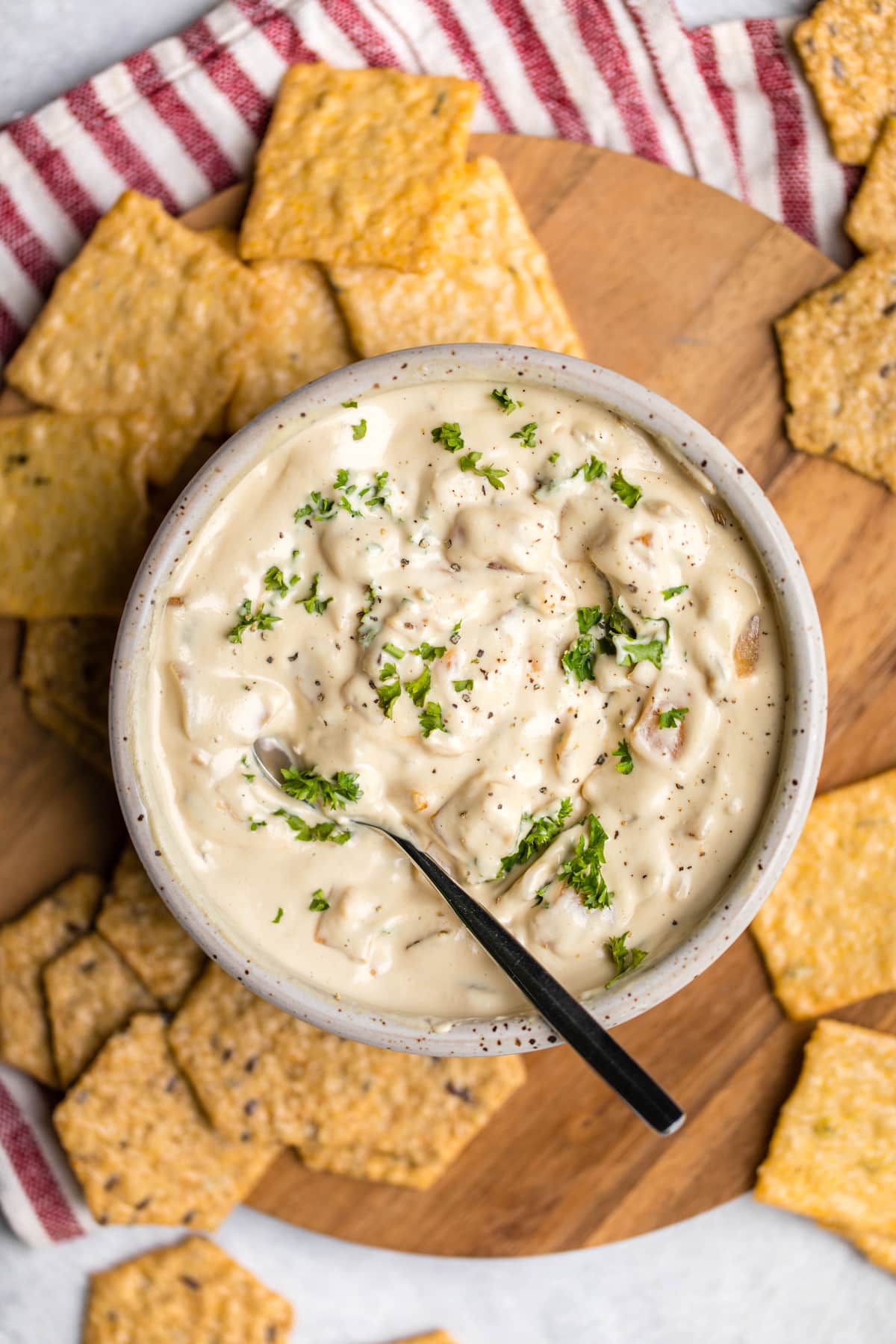 vegan french onion dip in white speckled bowl topped with fresh parsley and served with crackers