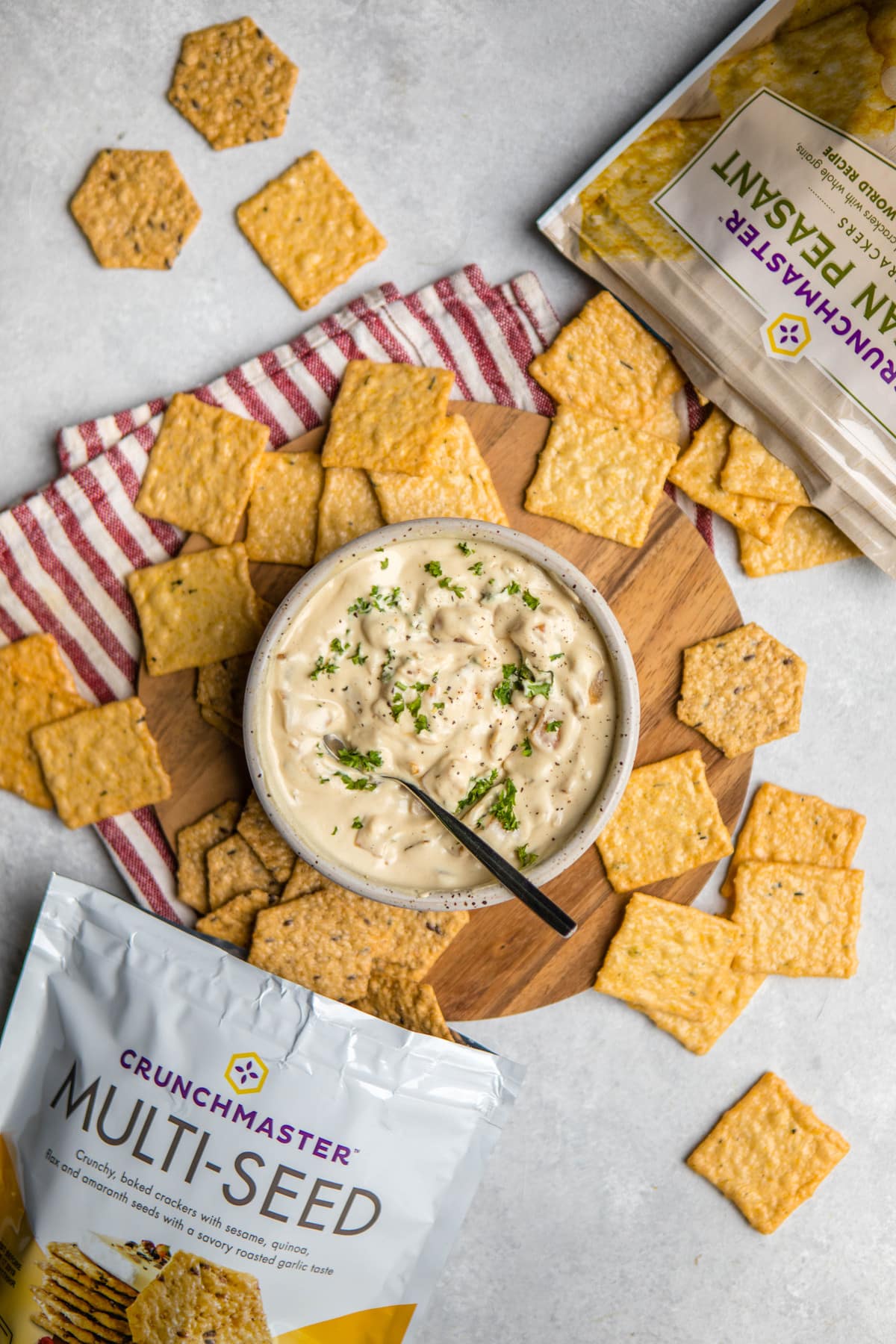 crunchmaster crackers spread on grey marble backdrop with bowl of vegan french onion dip