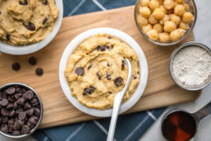 white bowl filled with chocolate chip chickpea cookie dough on wooden serving tray