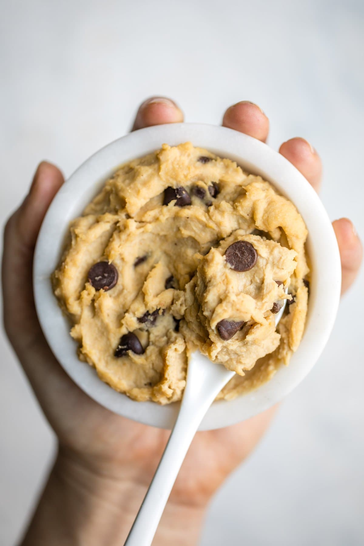 hand holding white bowl filled with chocolate chip chickpea cookie dough