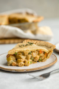 side view of slice of chickpea pot pie filled with chickpeas, peas and carrots on white speckled plate with silver fork