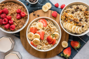 three white bowls of oatmeal topped with various toppings