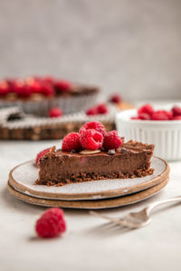 slice of no bake chocolate raspberry tart on white speckled plate
