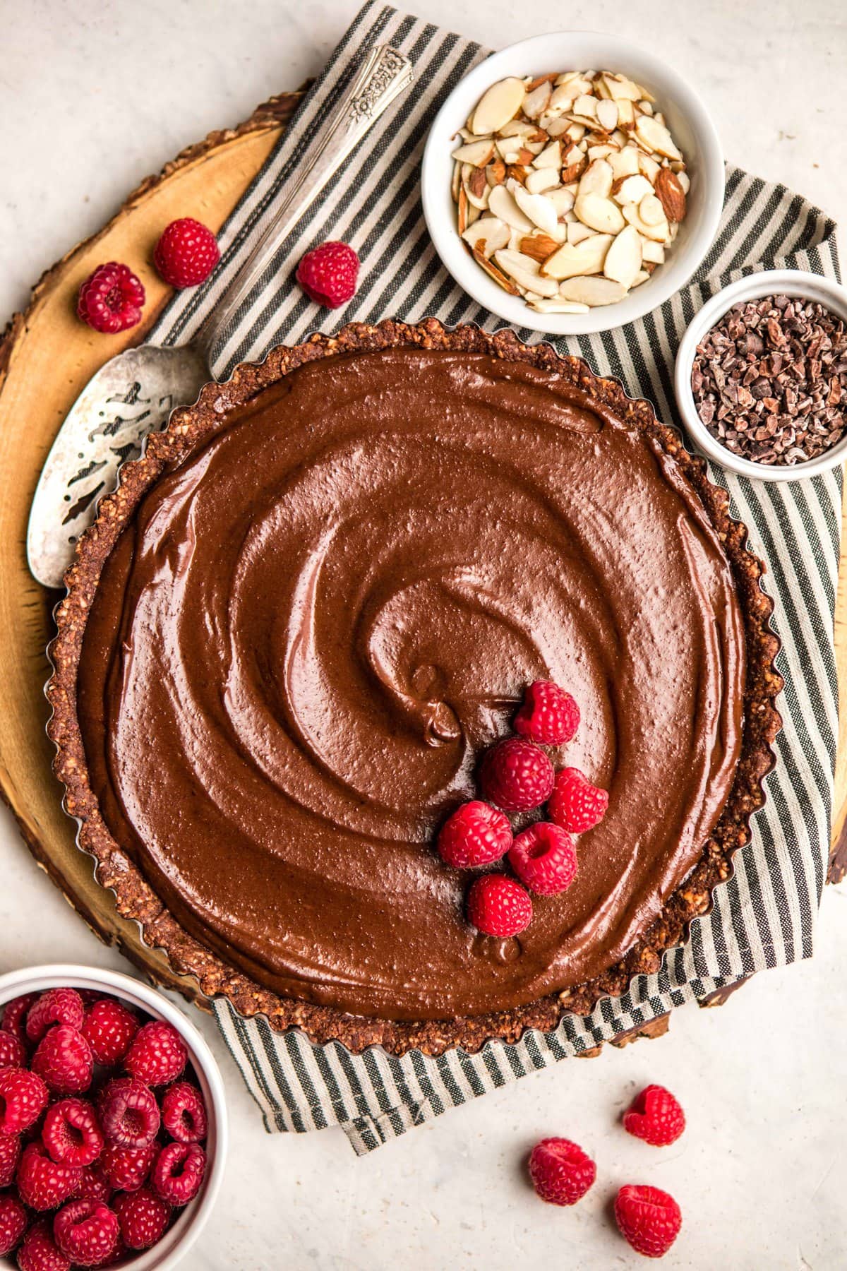 no bake chocolate tart in pie tin being topped with fresh raspberries 