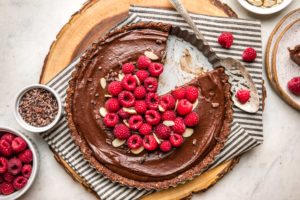 no bake chocolate raspberry tart with slice cut out of it on black striped napkin on round wood serving tray