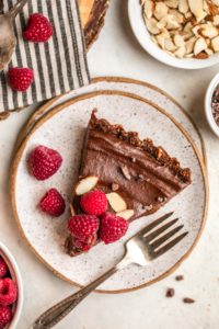 slice of no bake chocolate tart topped witth fresh raspberries and almonds