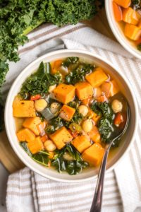 close up photo of sweet potato kale soup in white bowl with silver spoon