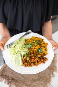 woman in black dressing holding plate of picadillo, arroz con guandules, and cabbage salad