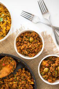 two bowls of vegan picadillo with skillet of picadillo and two silver forks