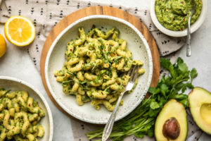 white speckled bowl filled with pesto pasta and topped with fresh basil