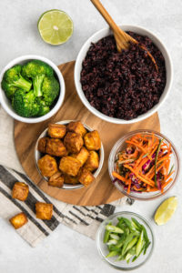 ingredients for black rice bowls in small glass bowls arranged on gray stone backdrop