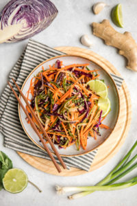 bowl of crunchy asian slaw surrounded by ingredients to make slaw