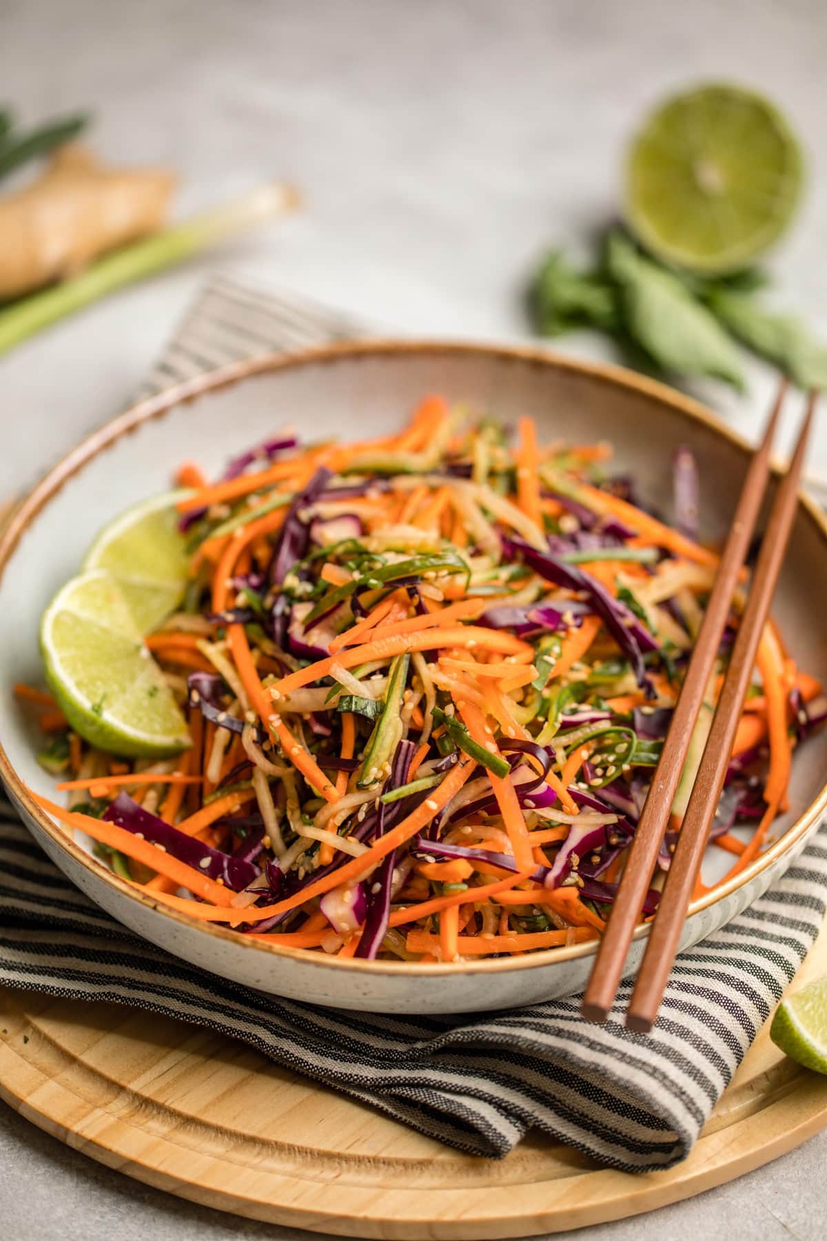 close up photo of crunchy asian slaw in white bowl with tan rim and wooden chopsticks
