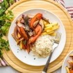 vegan lomo saltado with french fries and white rice on white plate topped with parsley