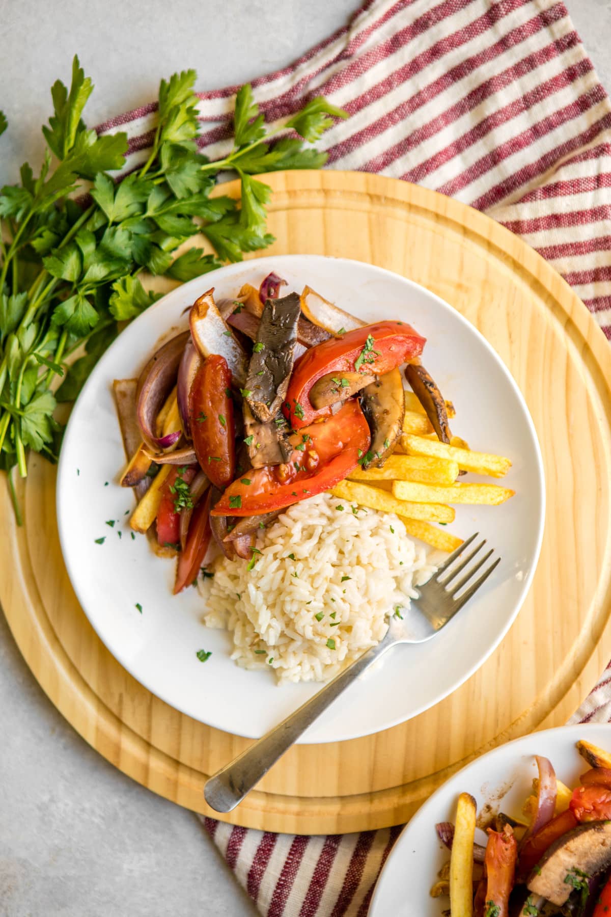 vegan lomo saltado with french fries and white rice on white plate topped with parsley