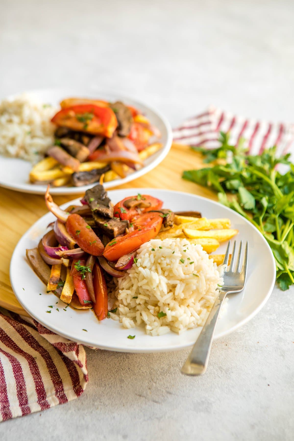 side shot of two white plates of lomo saltado with fries and rice