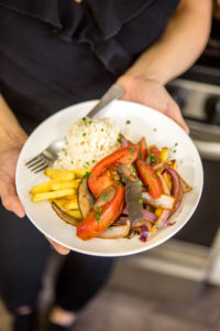 close up of chef ant's hands holding plate of lomo saltado