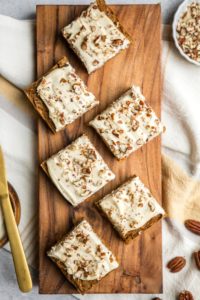 squares of frosted vegan carrot cake on wood serving plank