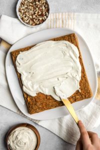 cashew cream frosting being spread on baked healthy vegan carrot cake with gold knife