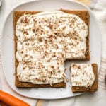 frosted healthy carrot cake topped with pecans on square white serving tray