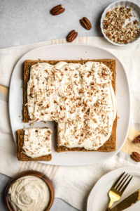 vegan carrot cake on square white plate with pecans scattered around it