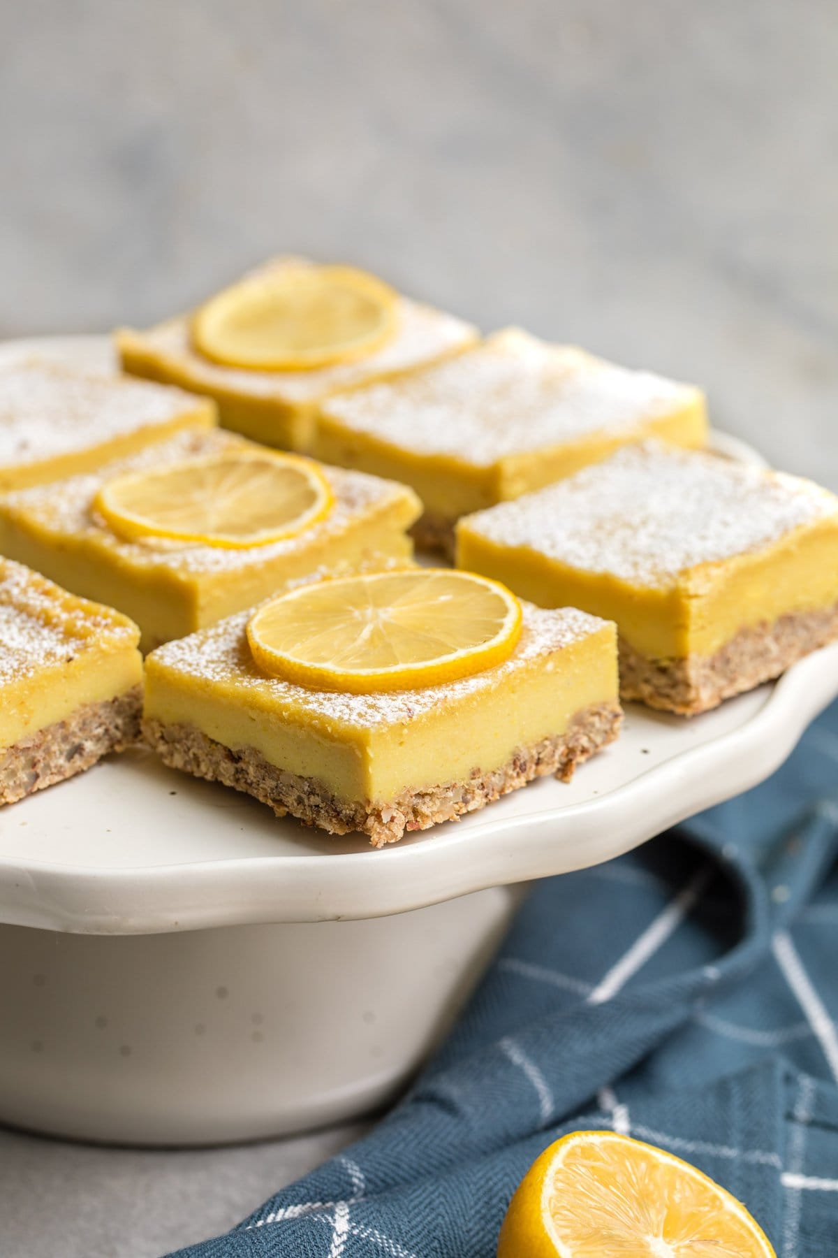 vegan lemon bars topped with powdered sugar on white serving platter with dark blue linen towel