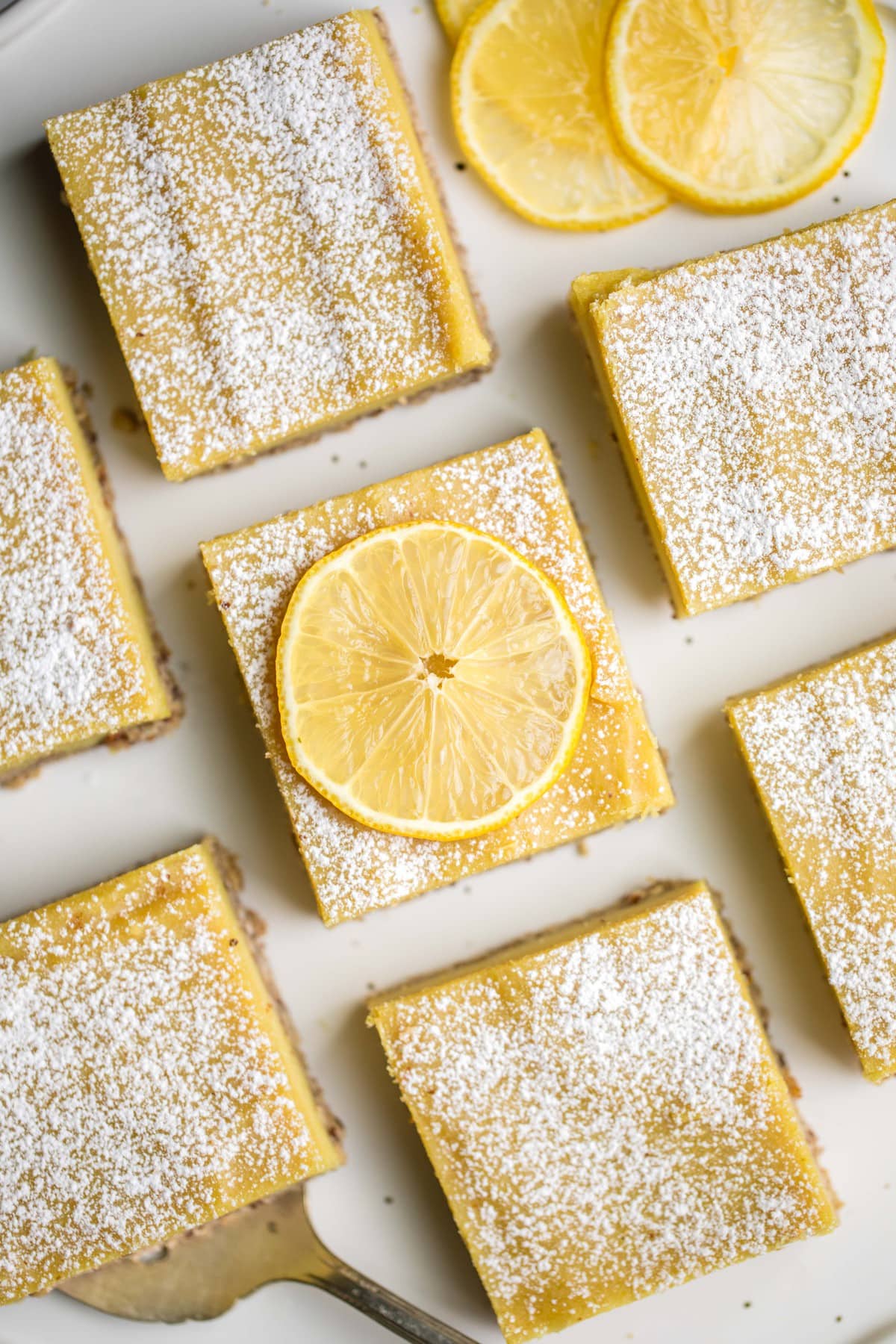 close up shot of lemon bars topped with powdered sugar and lemon slices on white background