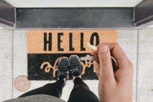 hand holding set of keys over brown "hello" doormat