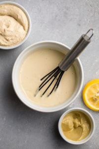 white bowl of hummus dressing with black whisk on gray background