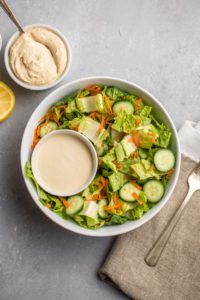 bowl of undressed salad with hummus salad dressing on the side