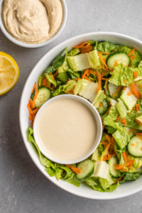 large salad bowl with small white bowl of hummus salad dressing on dark gray background