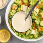 large salad bowl with small white bowl of hummus salad dressing on dark gray background