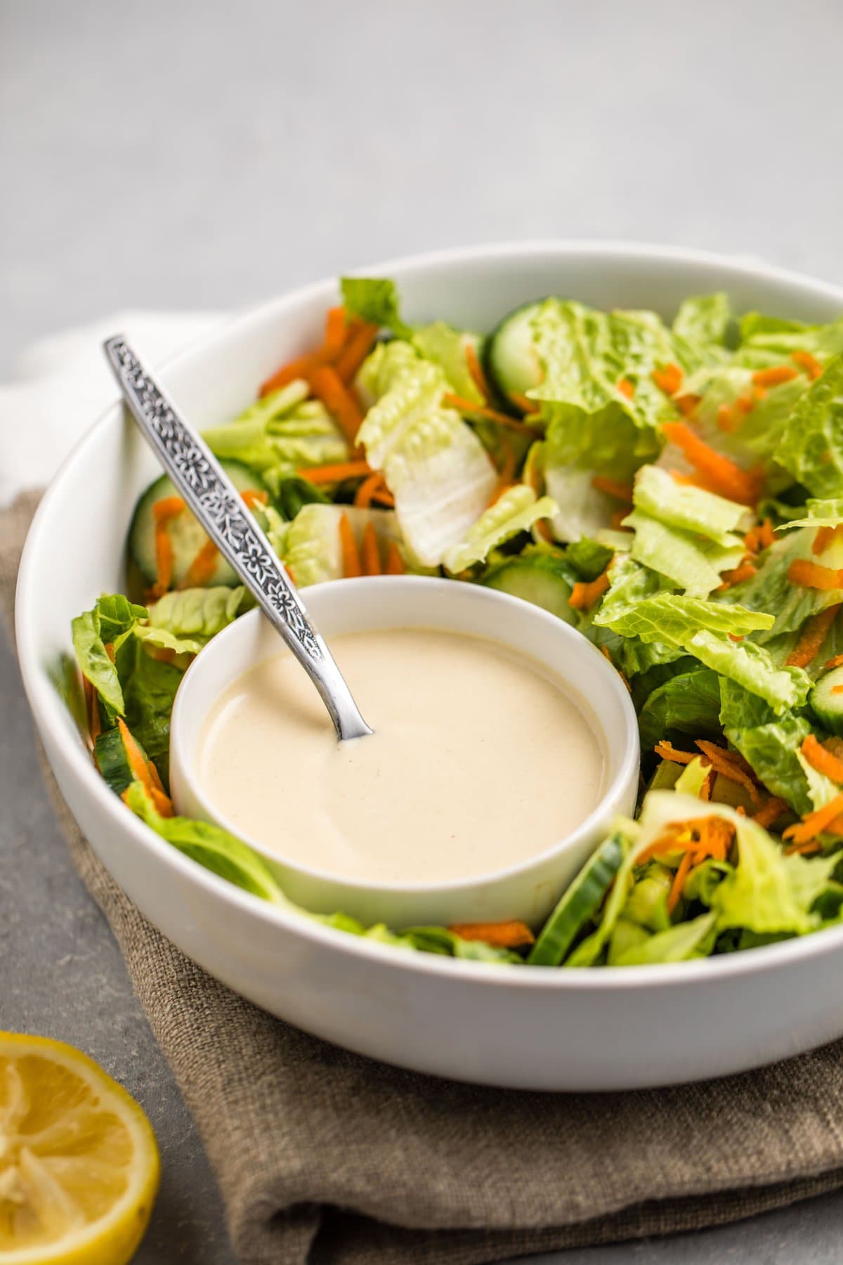small white bowl of hummus dressing in larger salad bowl