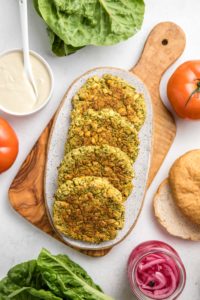 baked falafel burgers on speckled white serving tray surrounded by toppings