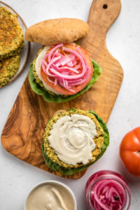two falafel burgers topped with tahini sauce on wood cutting board