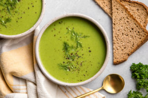 pea soup in speckled white bowl topped with fresh dill and golden spoon