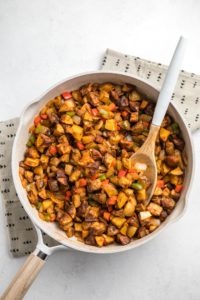 vegan breakfast potatoes and caramelized veggies in large white saute pan on white background