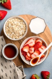 ingredients for strawberries and cream oatmeal arranged on round wood cutting board
